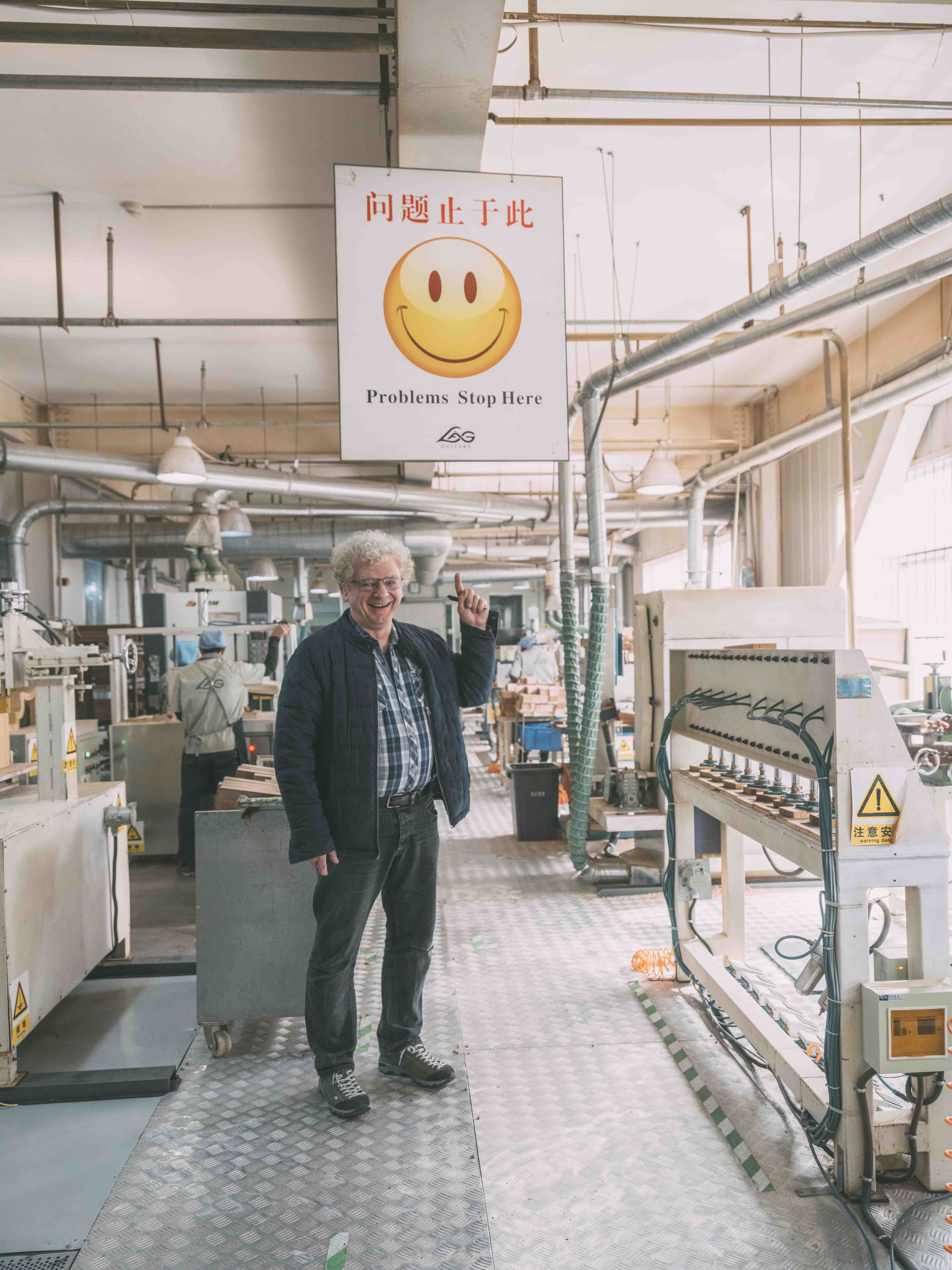 Maurice Dupont, luthier et Meilleur Ouvrier de France, montre un panneau sur lequel est inscrit, sous un Smiley, "Problems Stop Here, Lâg" à l'entrée de la chaîne de production de l'usine Lâg à Tianjin